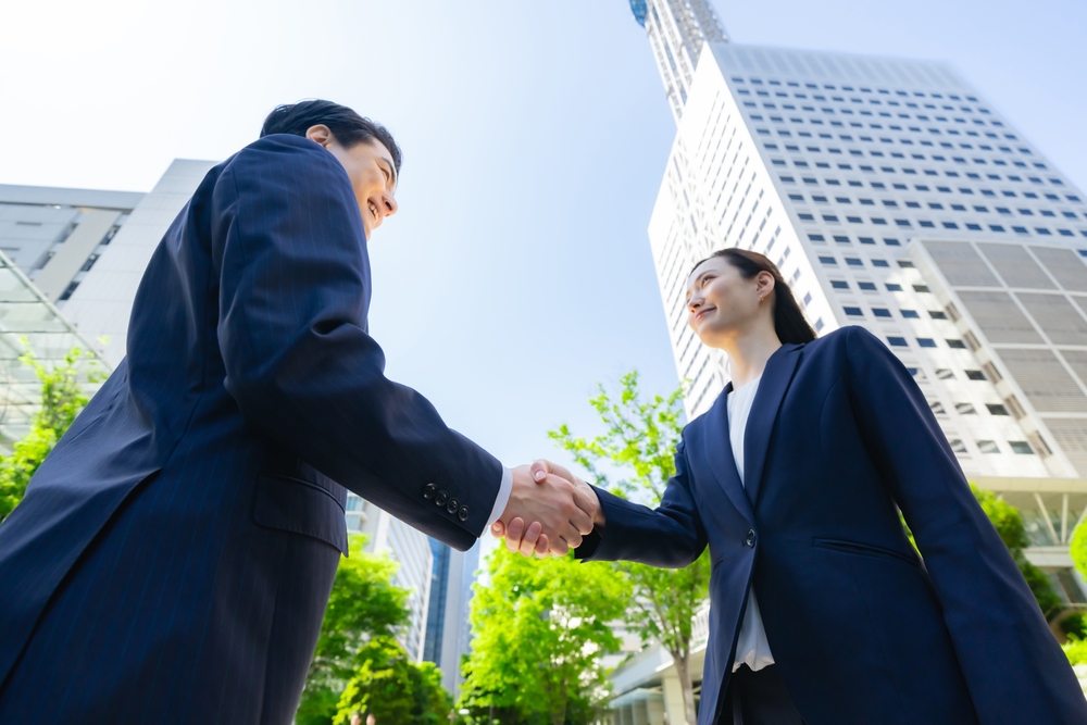 俯瞰の構図。ビルの前でスーツを着た男女が握手をしている写真。